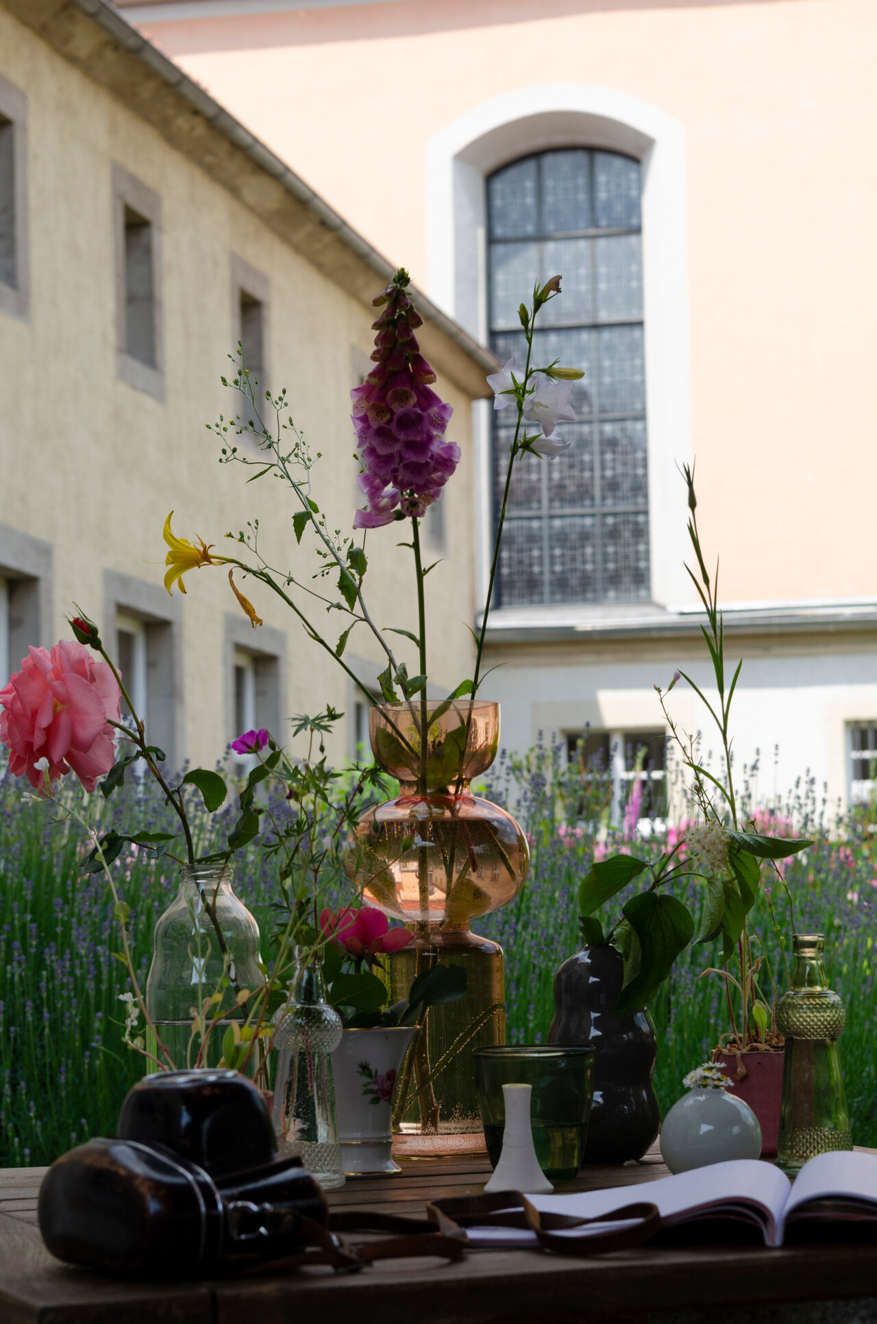 LÜCHTENHOF - Hofgarten - Stilleben von Blumen in Vasen, Fotoapparat und aufgeschlagenem Buch vor Kirche