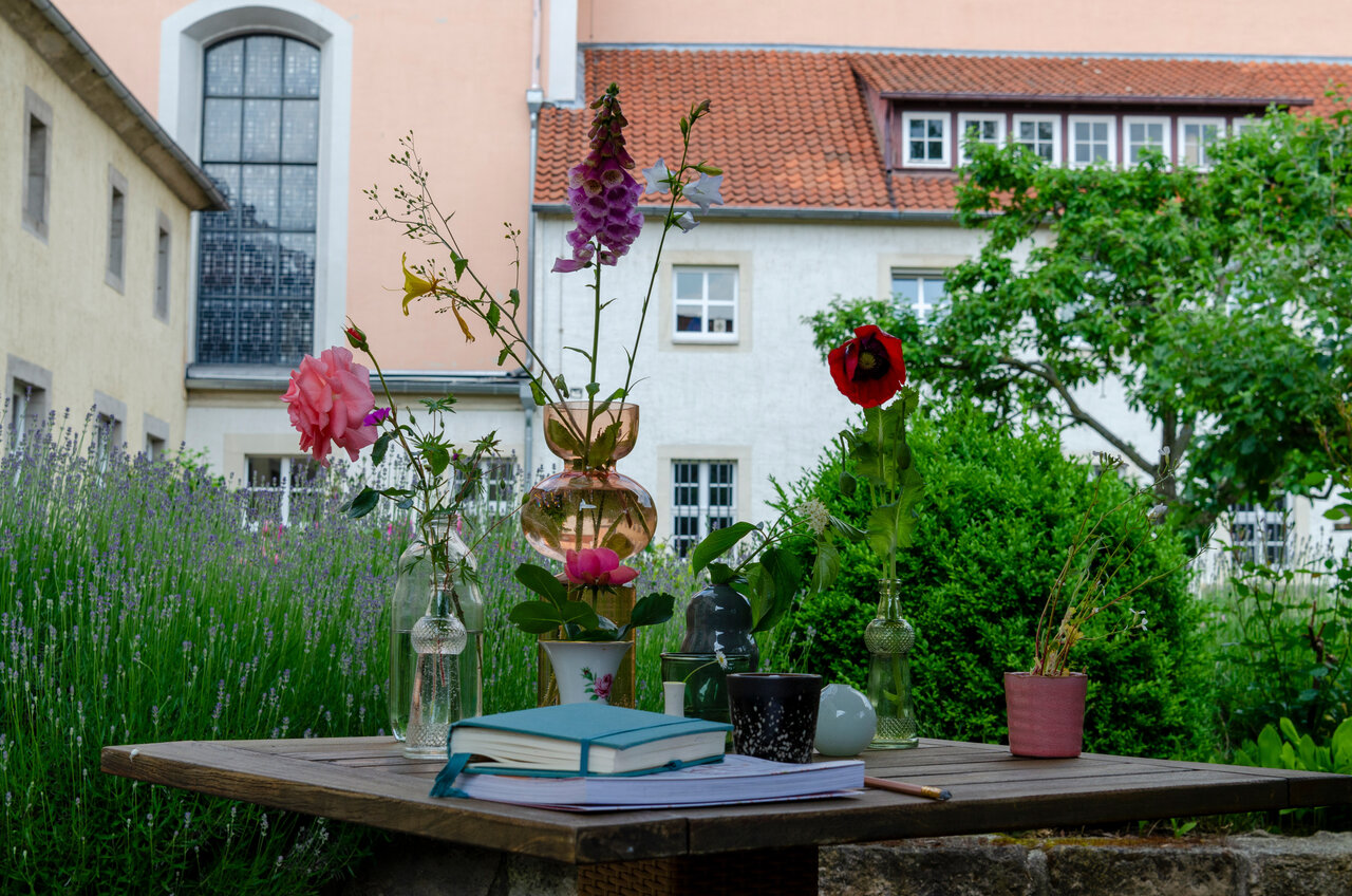 LÜCHTENHOF - Hofgarten - Stilleben von Blumen in Vasen, Tasse, Buch und Blick auf Kirche