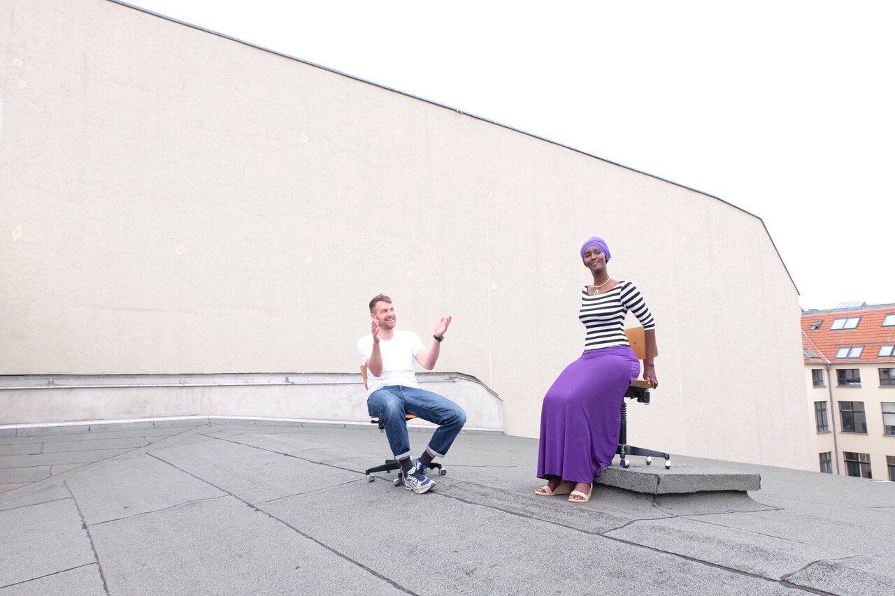 Fatuma Musa Afrah und Jon Hoekstra auf einem Häuserdach,  beide auf Drehstühlen sitzend